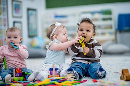 Tres bebés jugando con bloques y poniéndose juguetes en la boca.