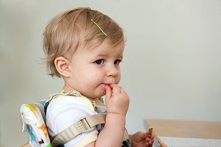 Niña pequeña con puntos rojos alrededor de la boca, comiendo en una mesa.