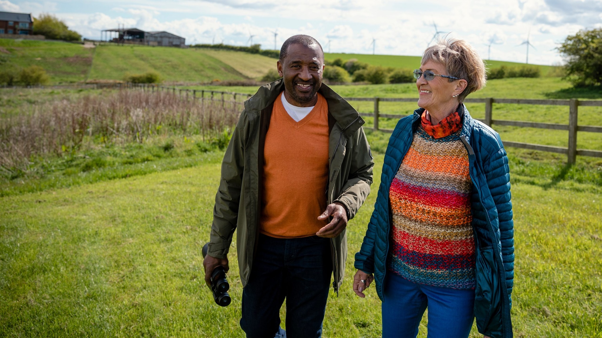 Two people walking and talking in a field in a rural setting.