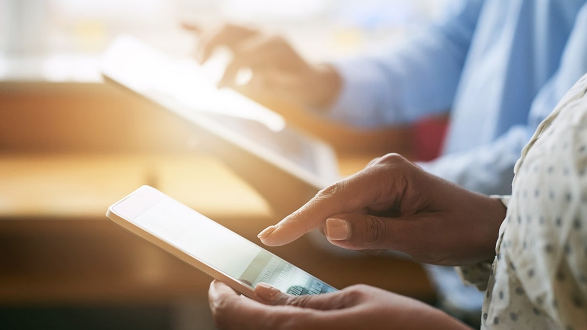 One person typing on a smart phone and one person typing on a tablet device.