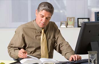 Man looking at a book while typing on a keyboard.