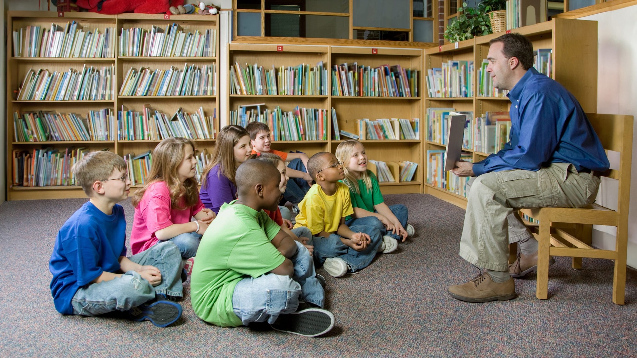 Teacher talking with a group of students in school library.