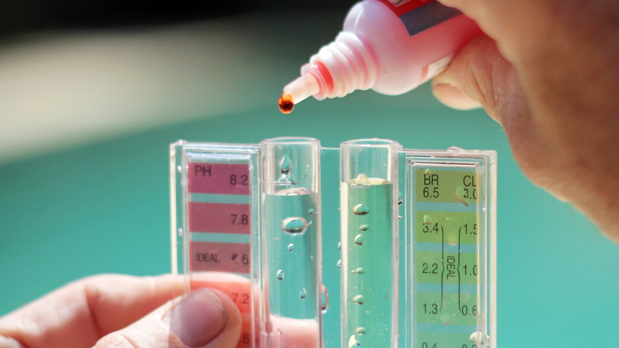 Close up of a person's hands holding a chlorine testing device in front of water.