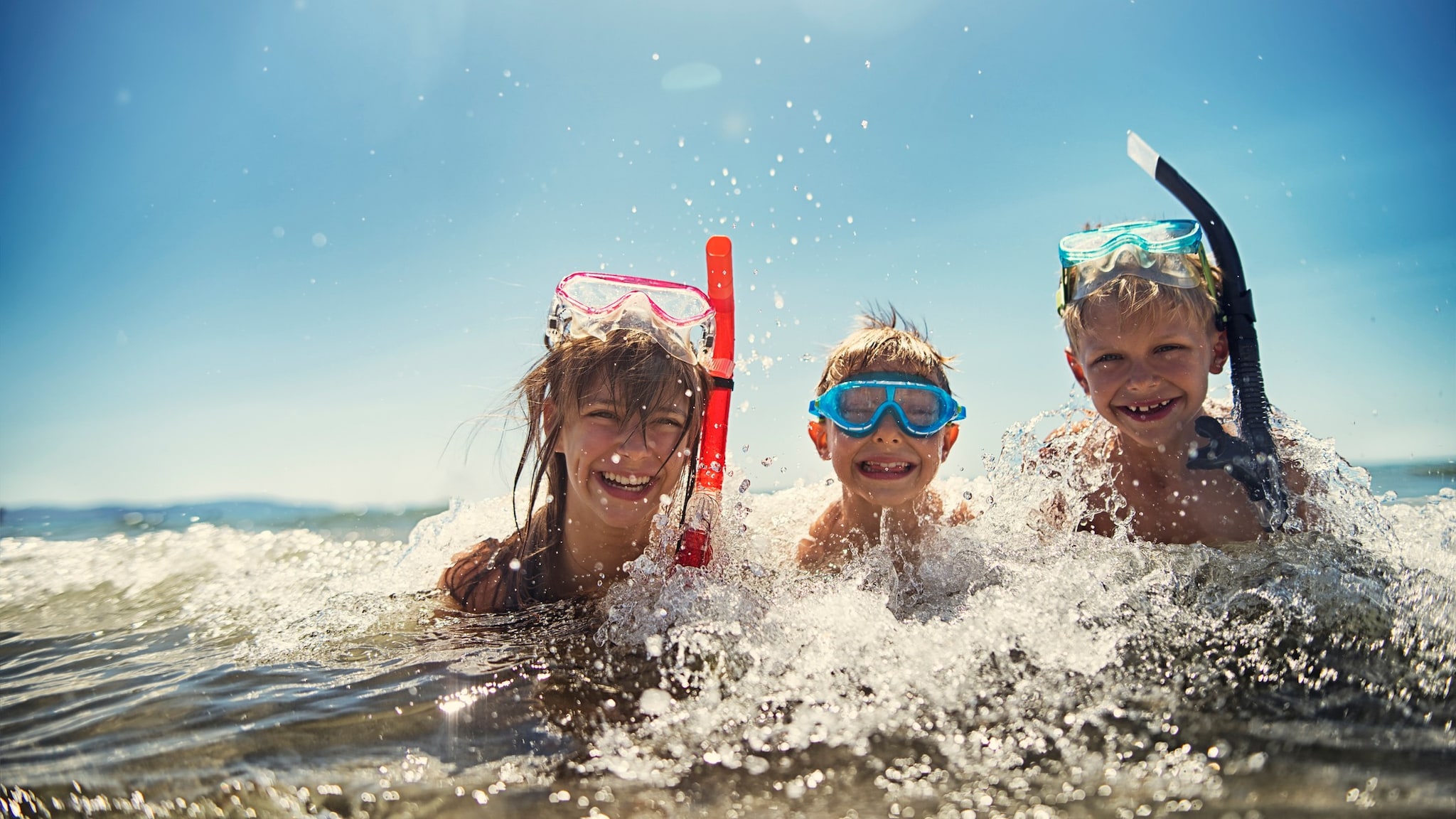 Tres niños sonriendo mientras están en el mar con equipo de esnórquel.