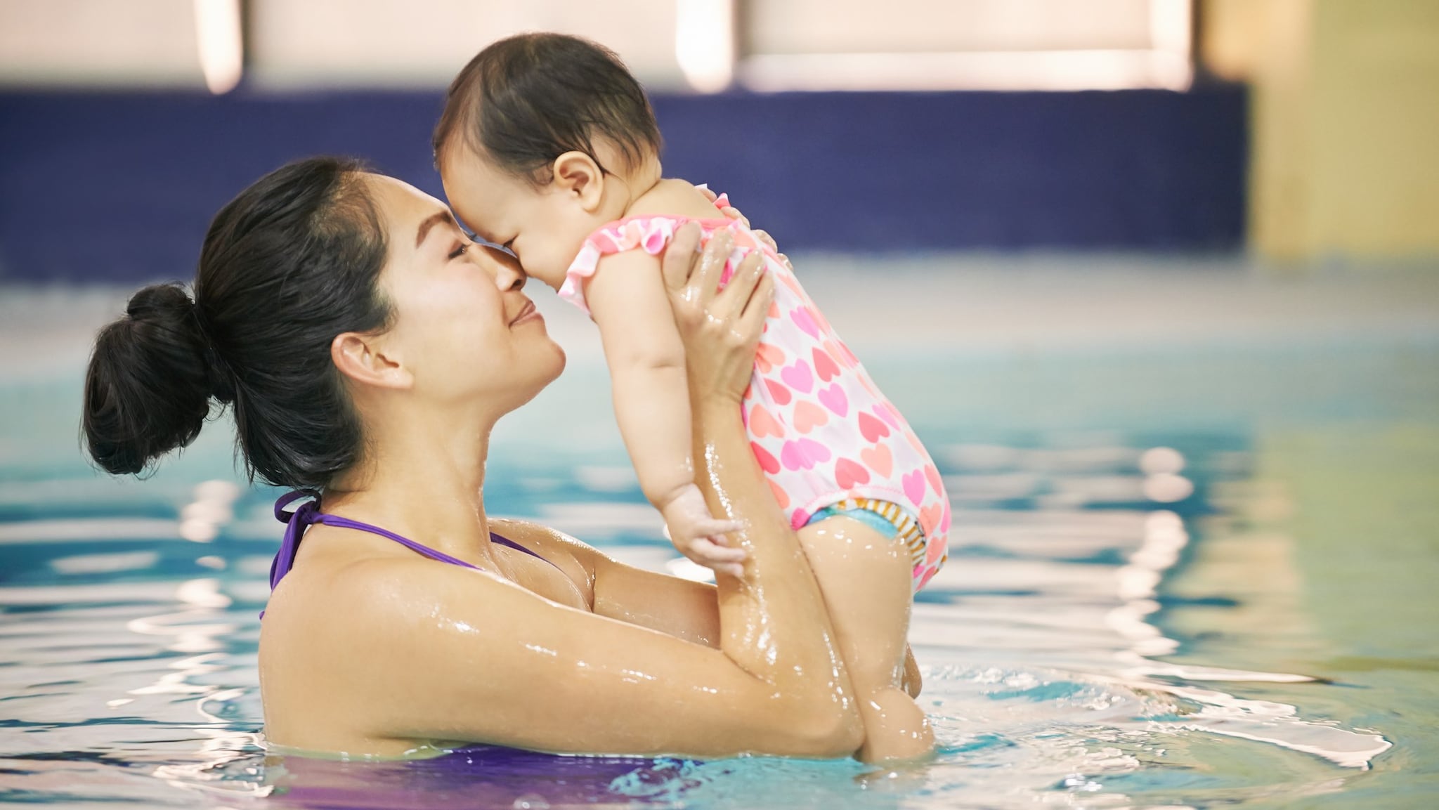 Madre en una piscina sosteniendo a un bebé que está usando un pañal para nadar.