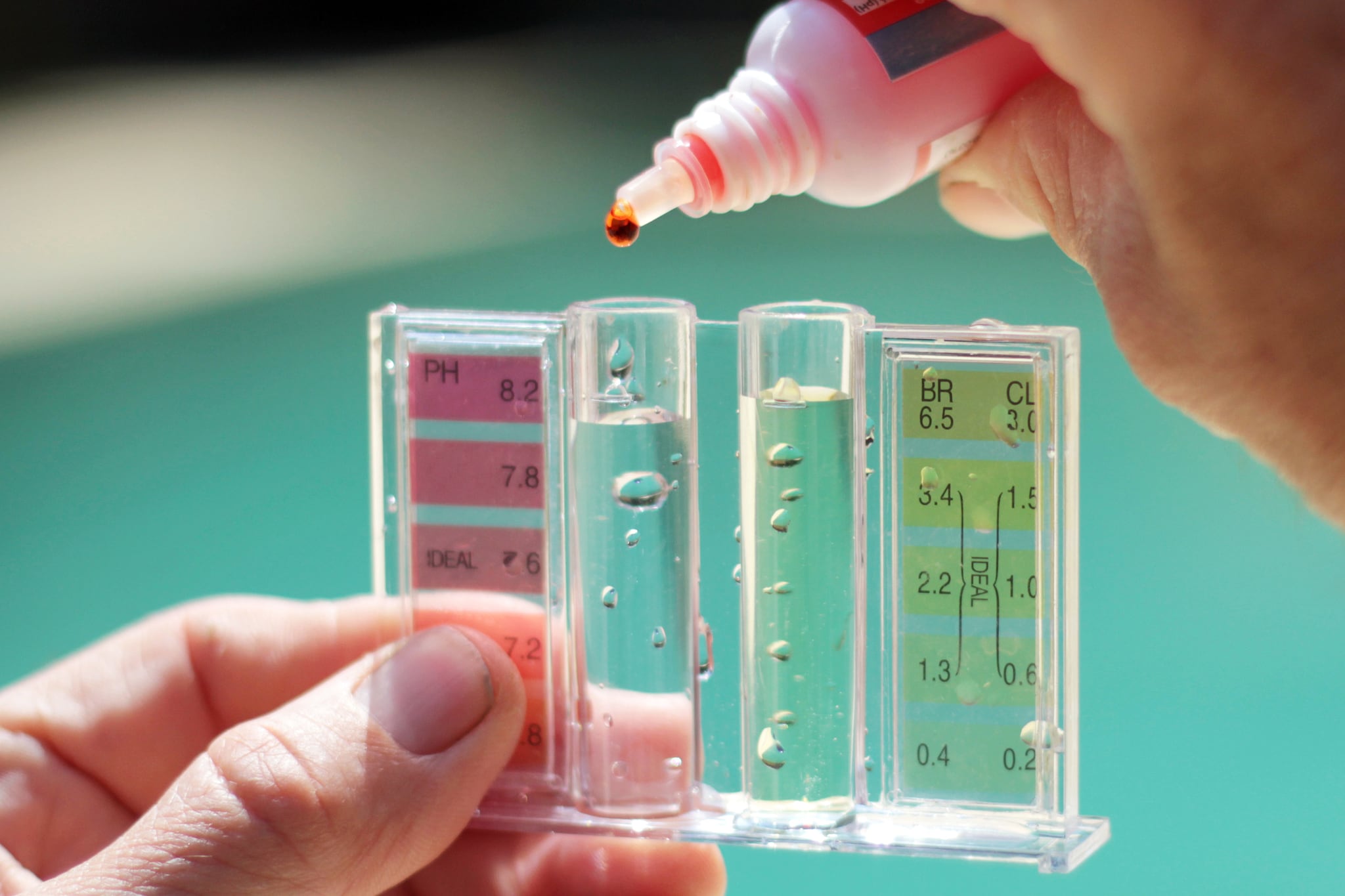 Close up of a person's hands holding a chlorine testing device in front of water.