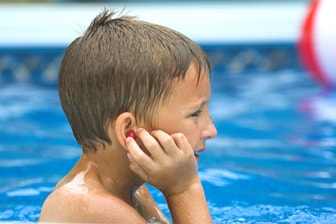 Niño en la piscina poniéndose tapones para los oídos.