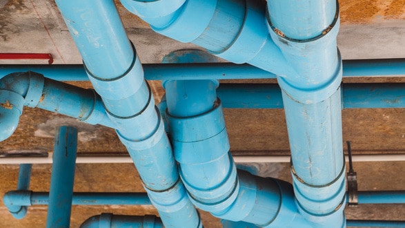 Blue pipes running in different directions at the top of an unfinished ceiling inside a building.