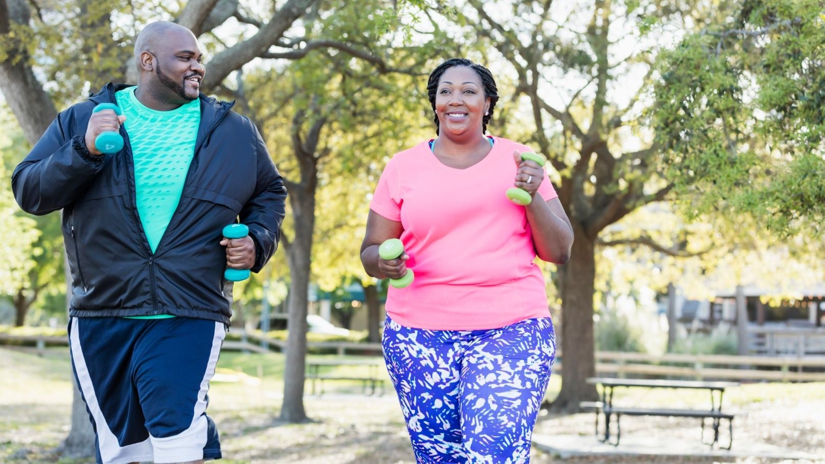 Two people walking in park and carrying hand weights.