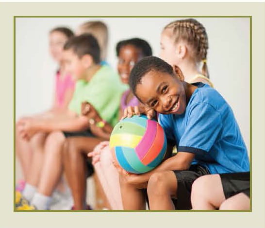 Young children sitting and smiling and holding a volleyball.