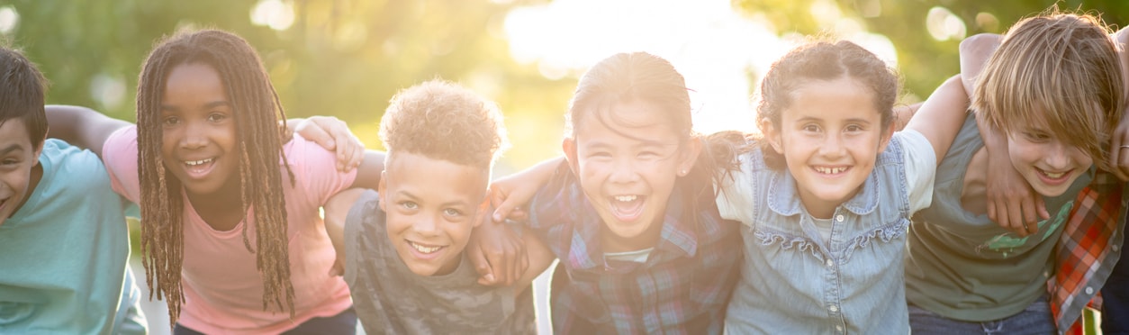 A multi-ethnic group of elementary age children huddled together for a photo. They are embracing each other while smiling and laughing.