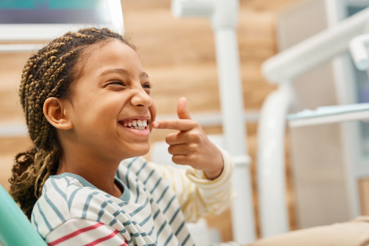 Young female child sitting on dental chair and showing her healthy teeth.