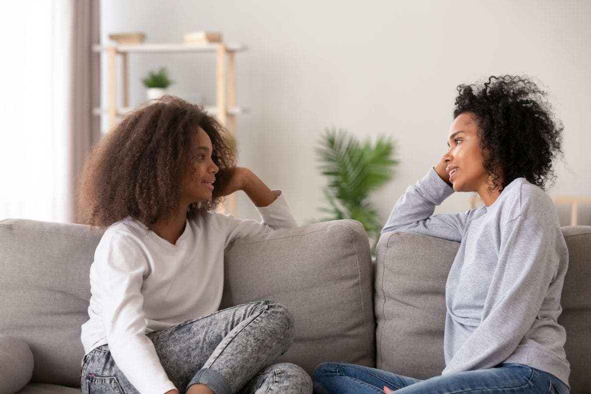 A mom listening to teen daughter sitting on couch together