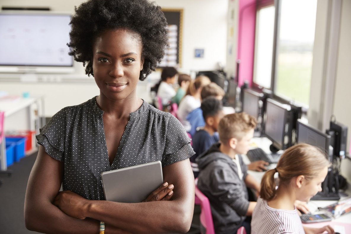 a teacher smiling in front of students in computer class