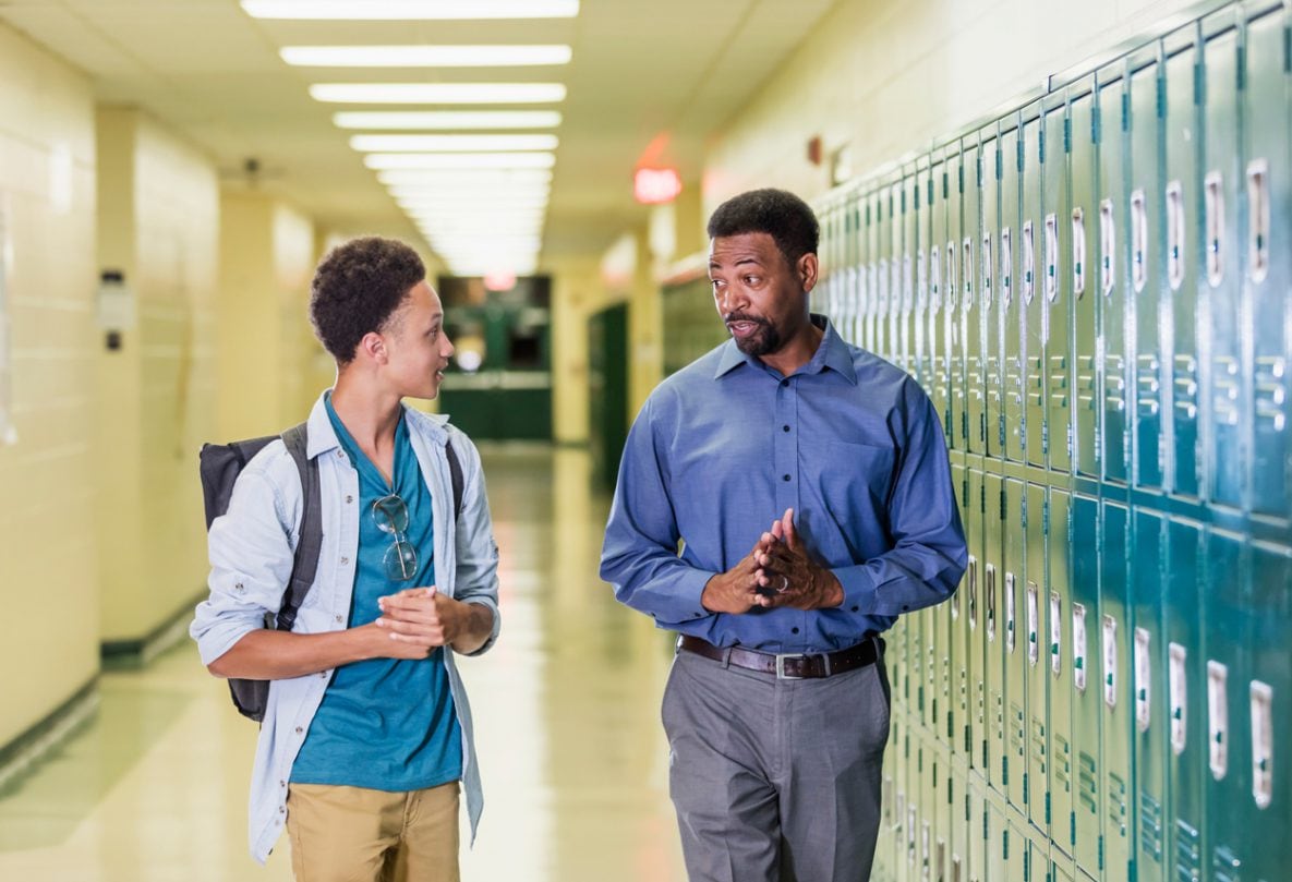 Teacher and teenage student walking in school hallway