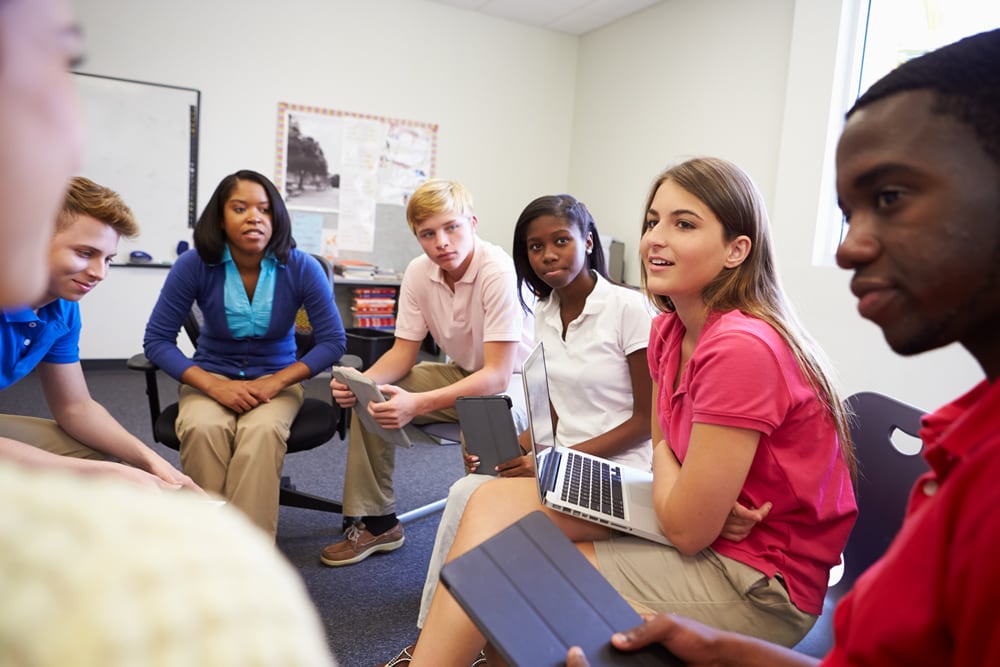 High School Students Taking Part In Group Discussion Sitting With Laptop