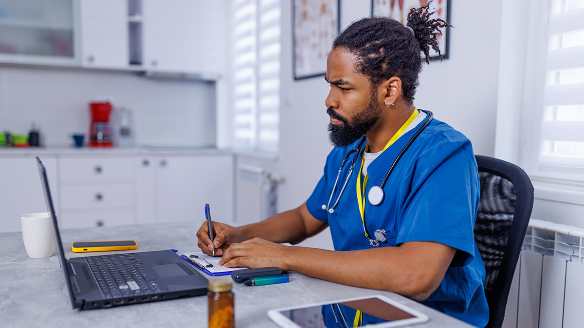 A health professional reviewing resources on a laptop while taking notes