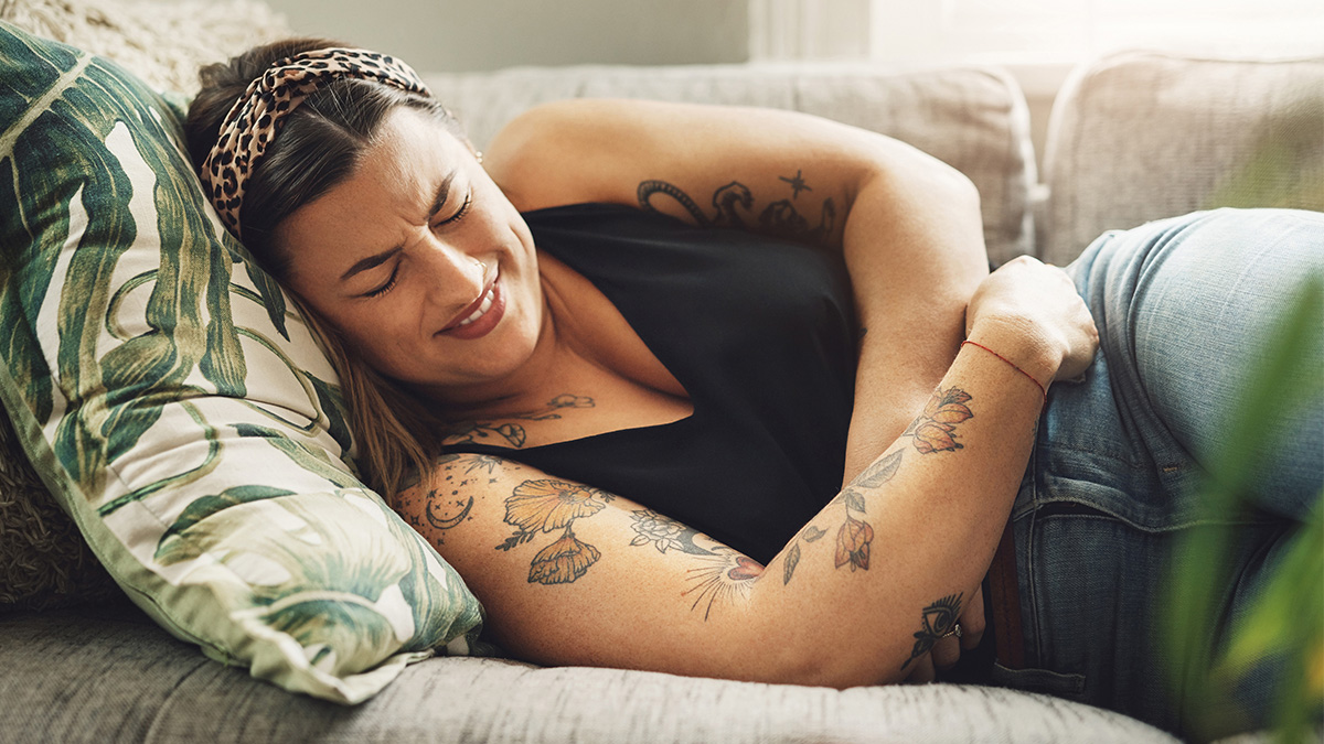 A woman grimacing in pain while laying down on a couch