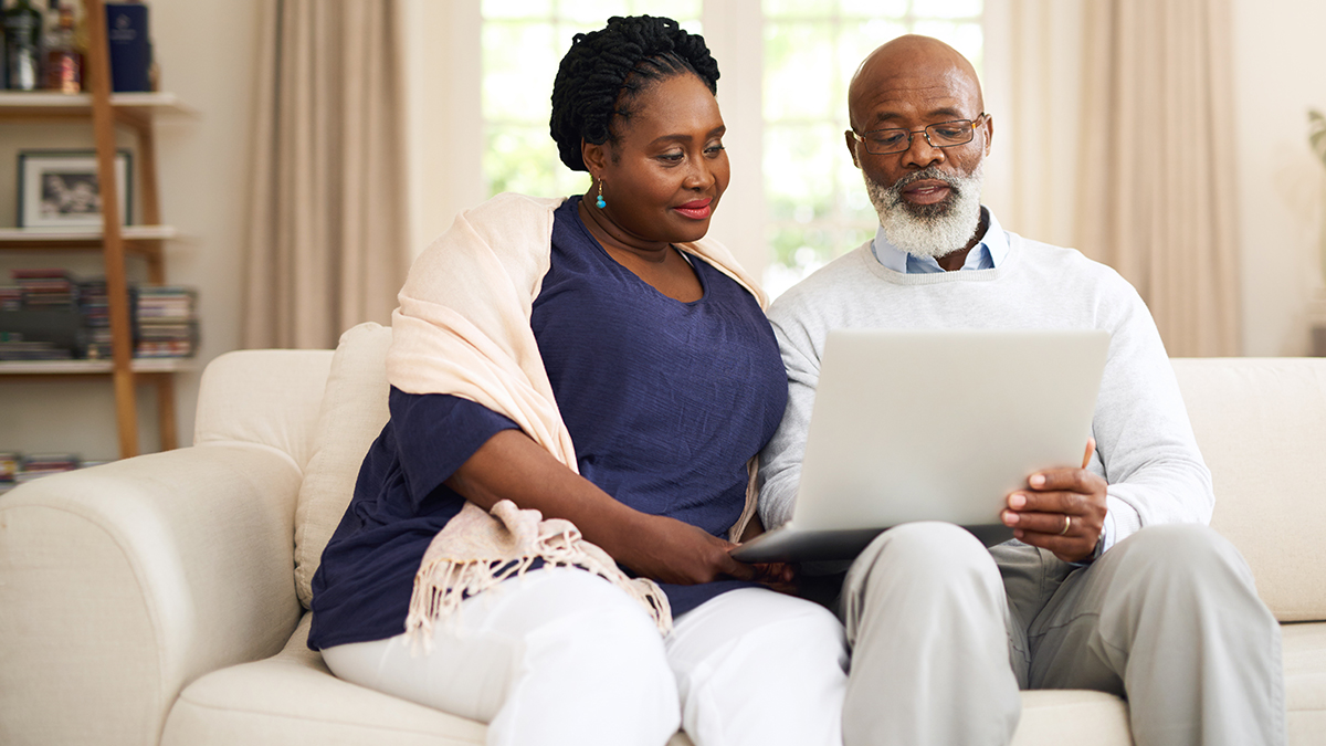 A man and a woman sitting on a couch and looking at a laptop together