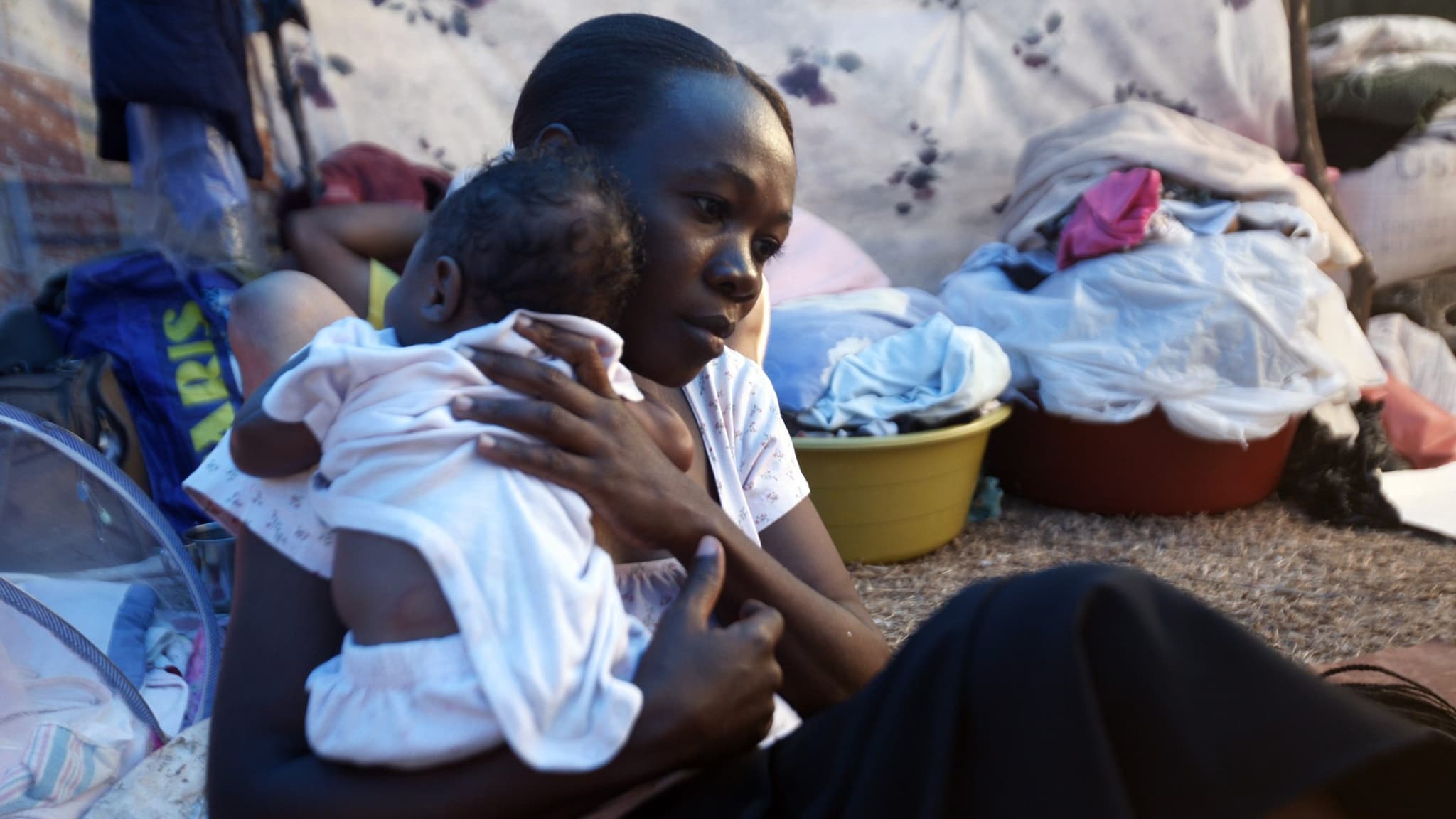 Mother comforts baby in a shelter setting.