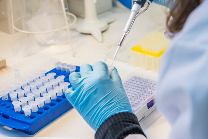 Scientist with blue glove puts a sample into a test tube to perform testing