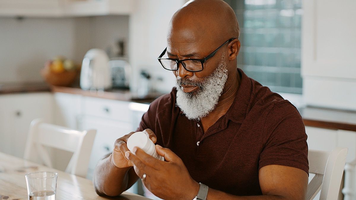 Senior African American man with bald head, white beard and glasses reading medicine bottle.