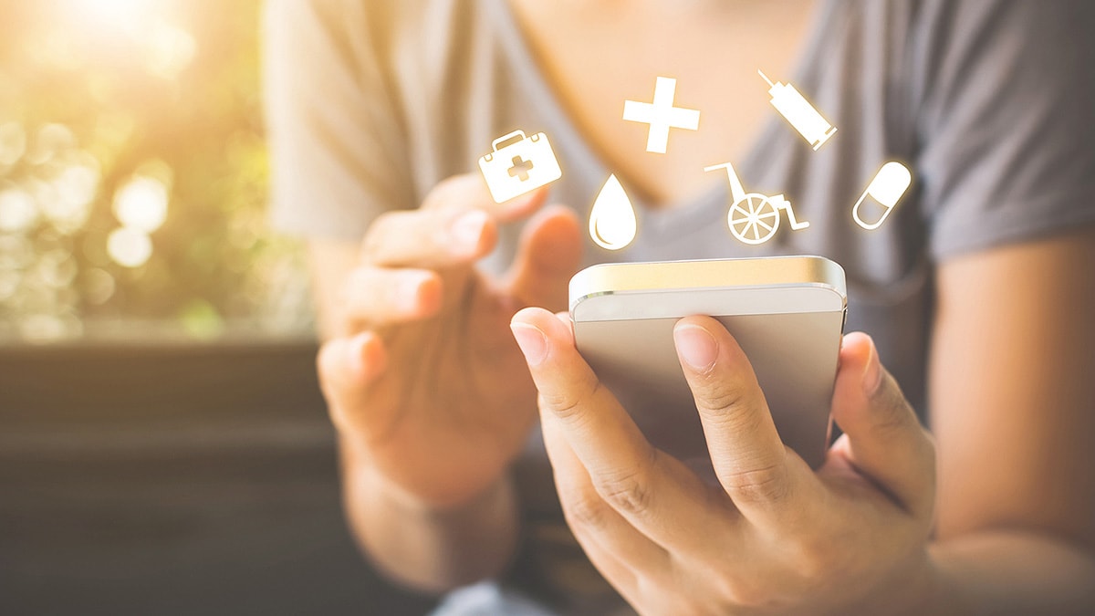 Woman using smartphone as medical icons such as the medical cross, a needle, and pill icon hover above.