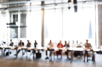 A blurred out row of people sitting at a long table in a meeting