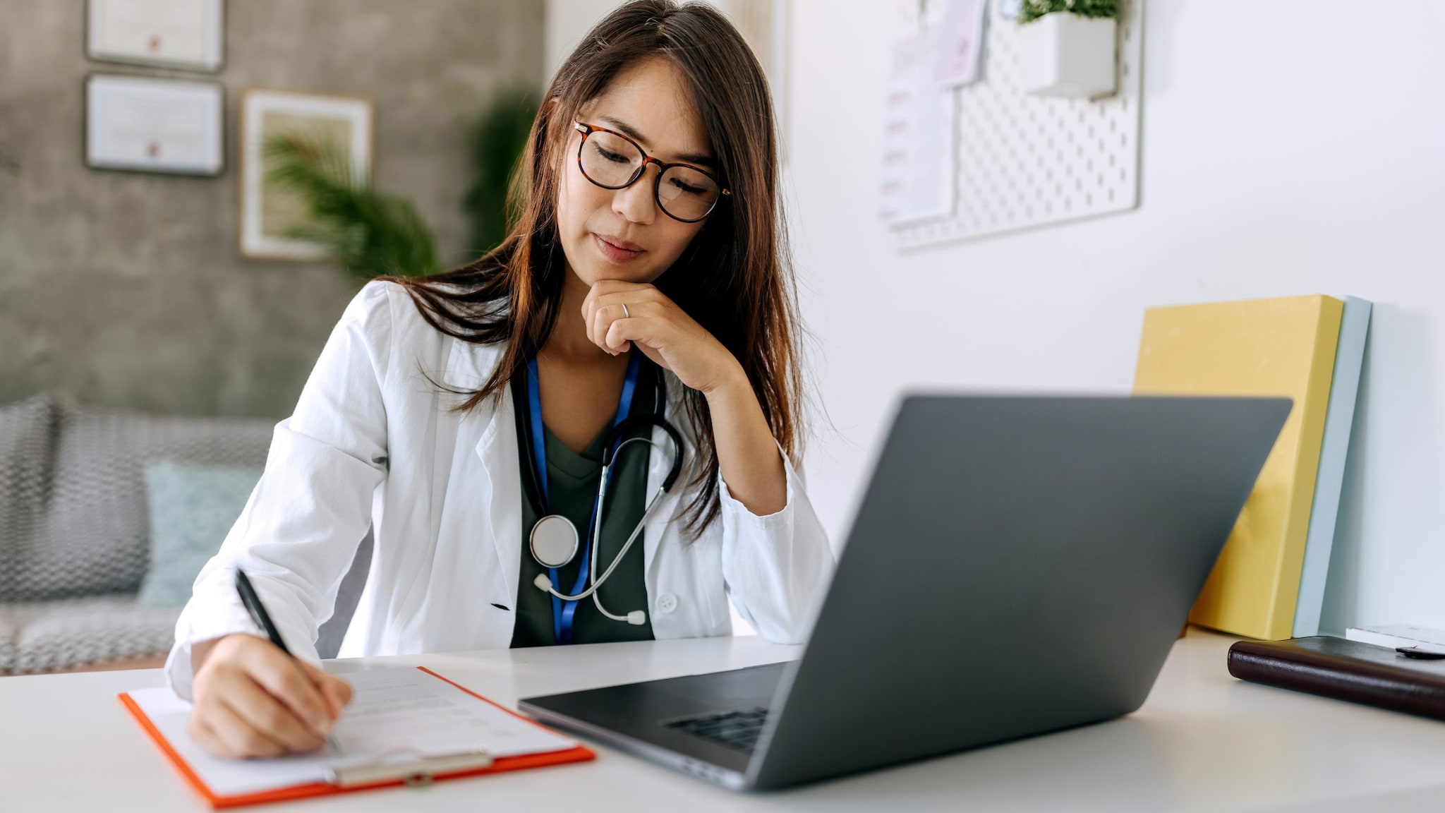 Healthcare provider takes note on a clipboard next to a laptop.