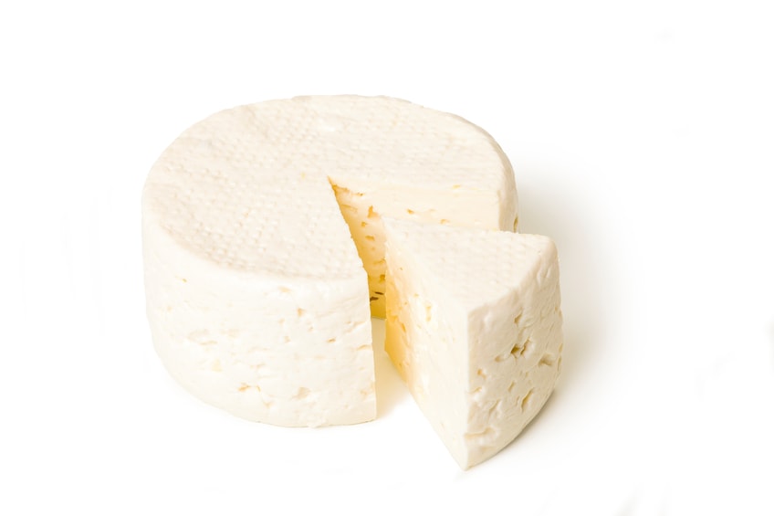 Round block of soft white cheese with one slice cut.