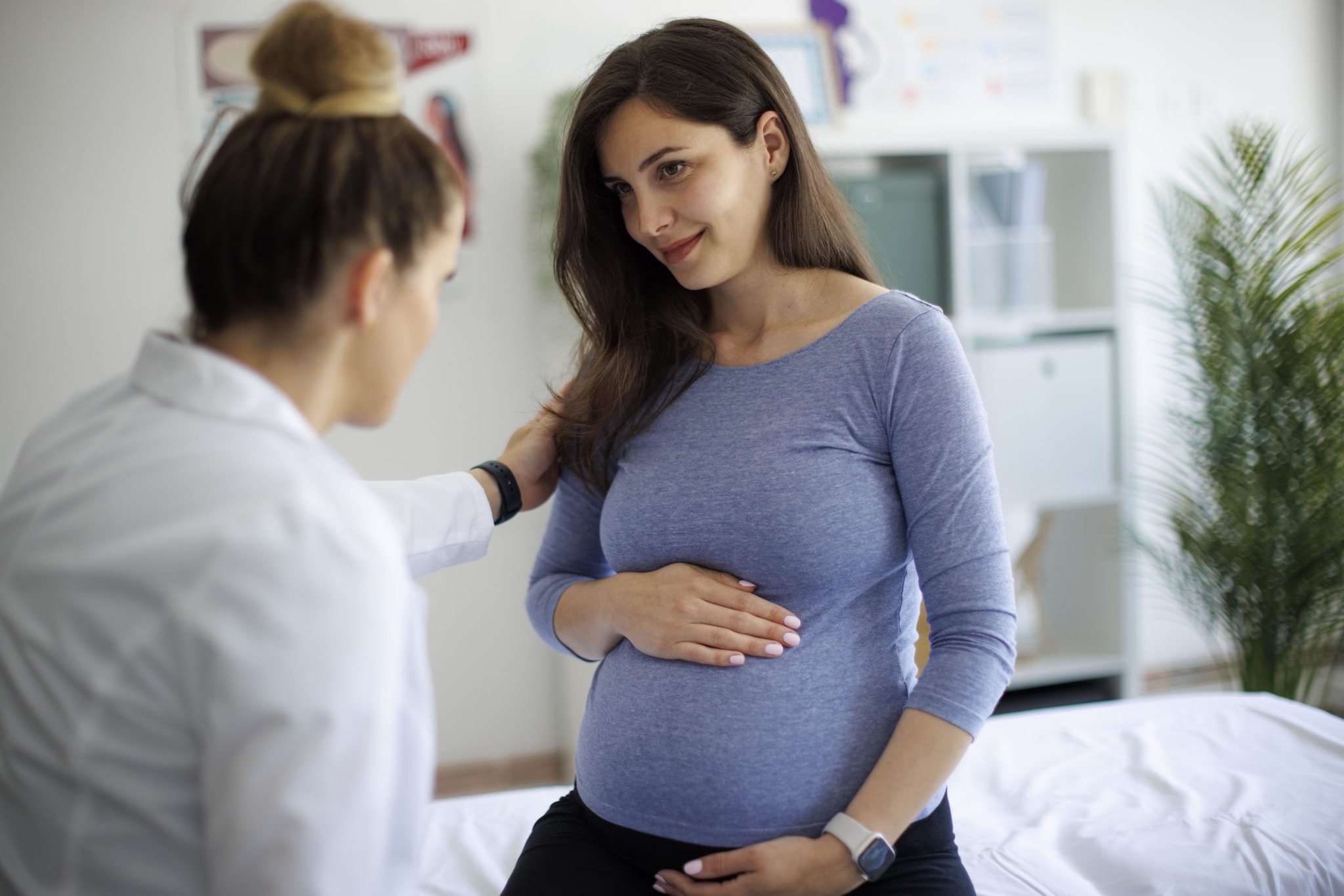 Pregnant person holding their stomach with their hand speaking to a doctor.