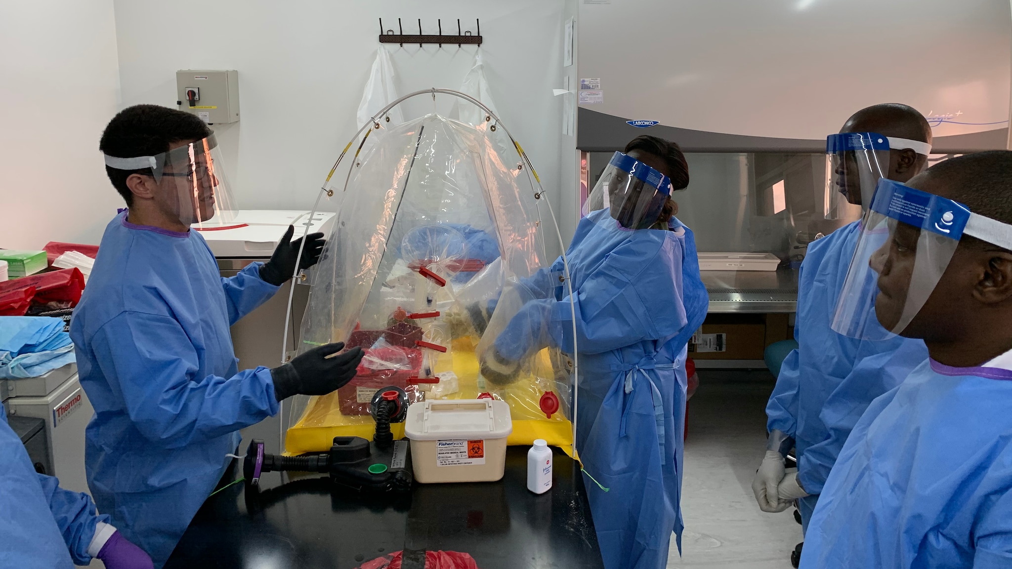 An LLS fellow (left) trains laboratory partners on infectious disease testing assays and how to remain safe with protective personal equipment.