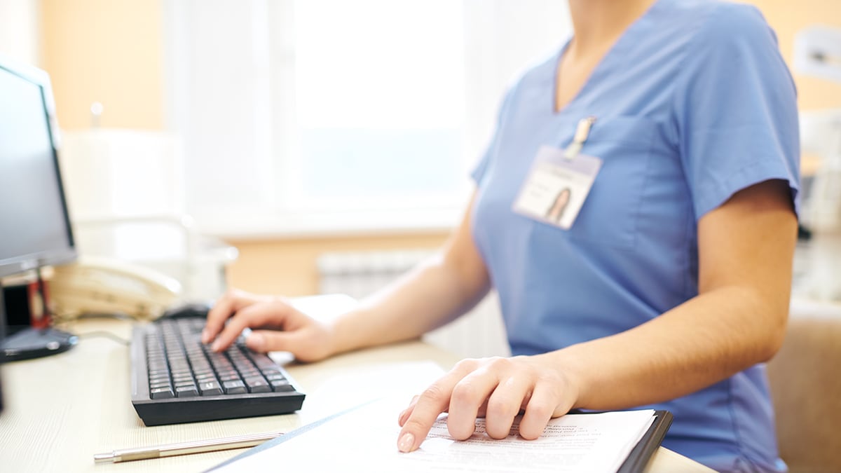 Woman in scrubs at computer.