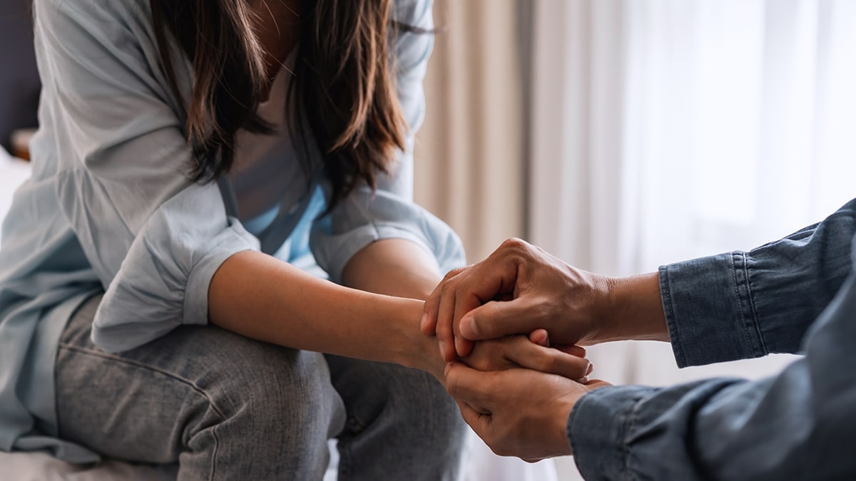 Young man comforting and supporting a sad woman by holding hands.