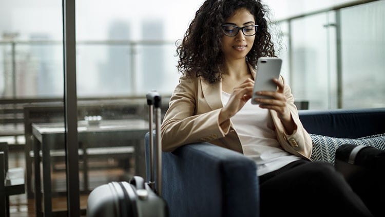 A female traveler holding a phone and sitting beside her suitcase.