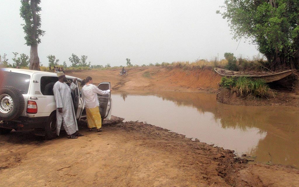 A woman and a village man stand out side of a car near a river.