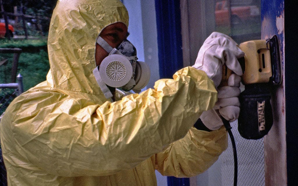 A man in a personal protect suite removing old, lead-based paint.