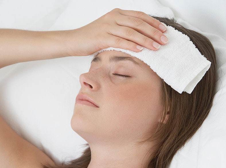 A woman lying in bed with a wet cloth on her forehead.