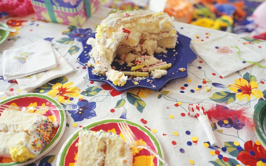 A number of party plates with birthday cake on a decorated table.