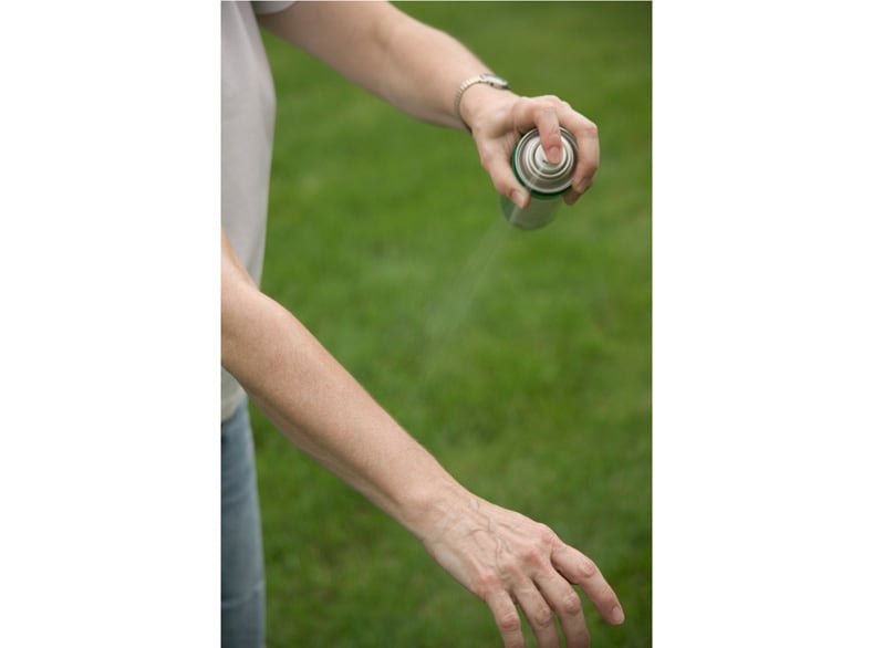 A person spraying mosquito repellent on their arm.