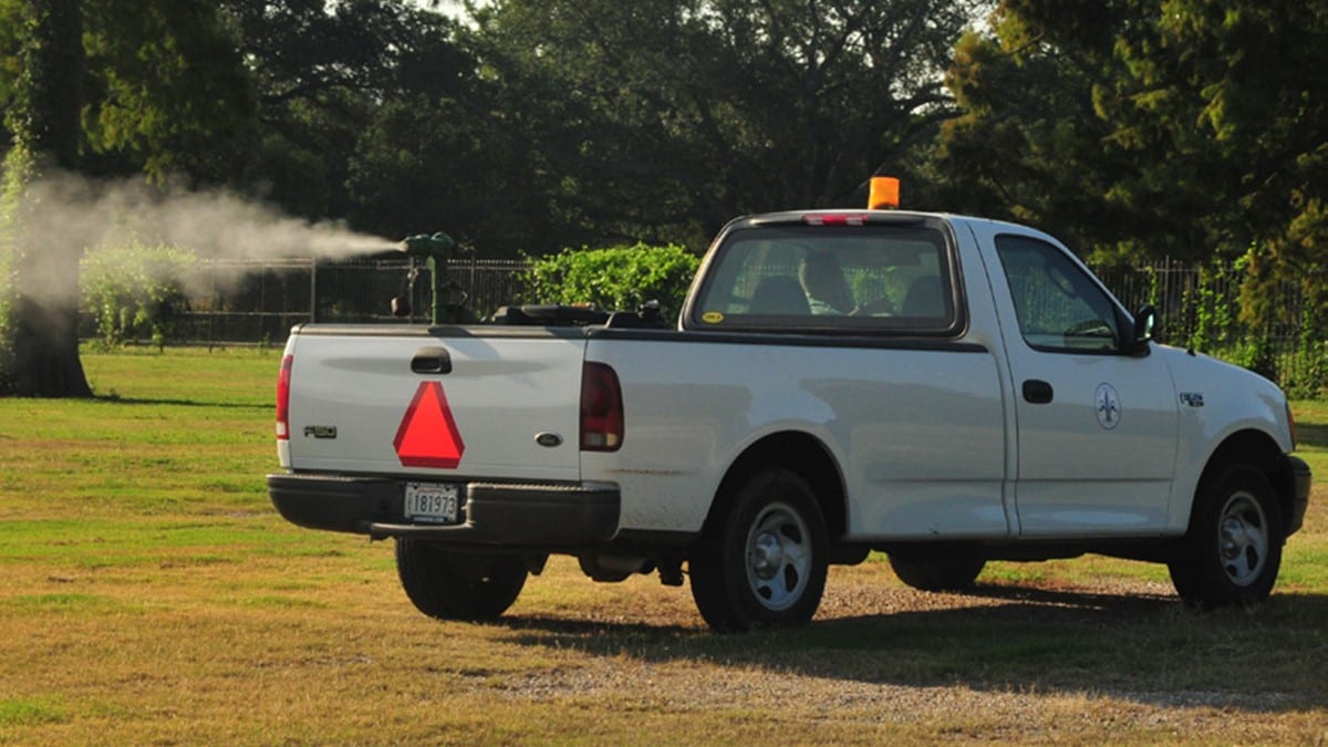 Camioneta de control de mosquitos rociando insecticida en el aire.