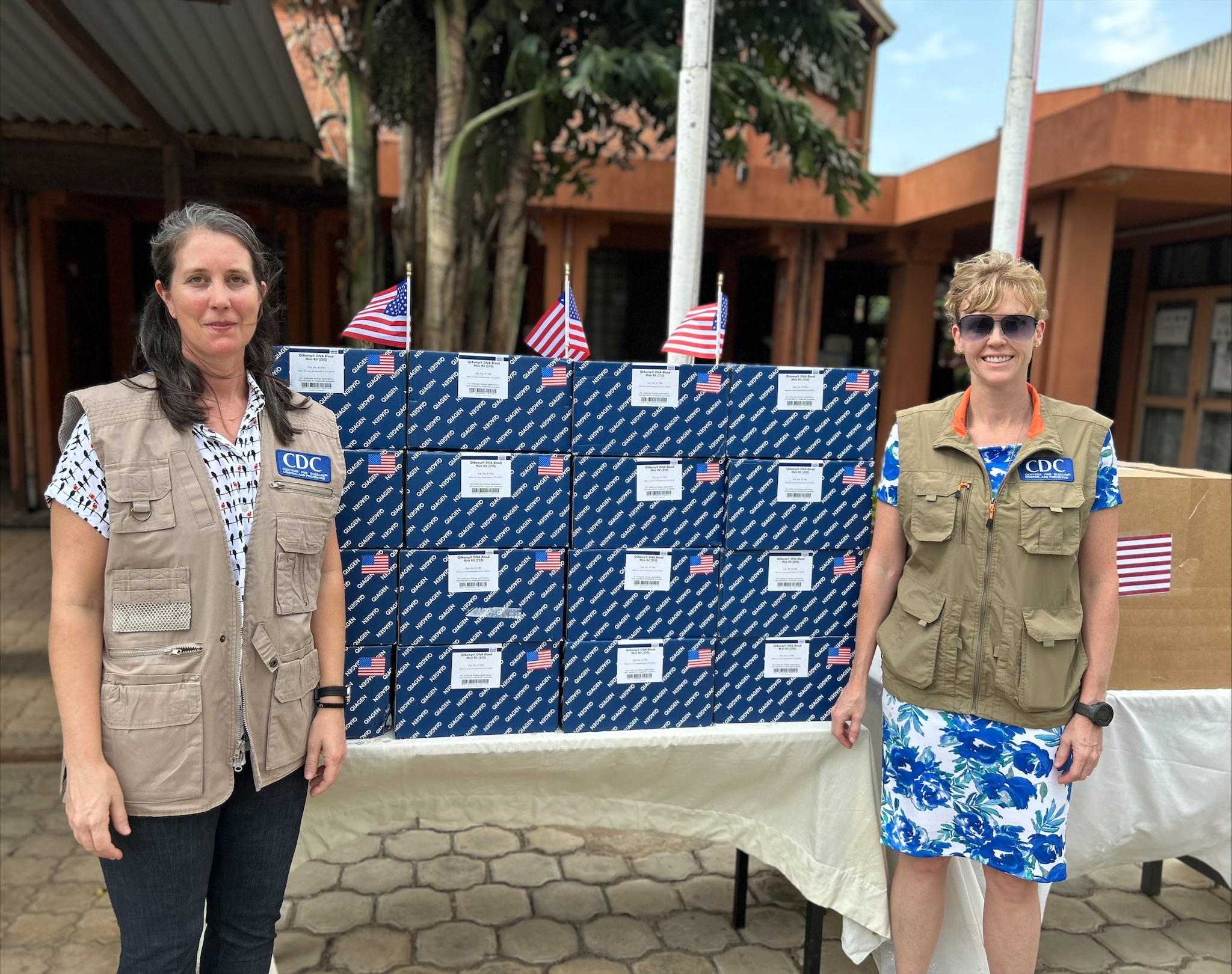 two women stand by a table covered in boxes, which contain laboratory testing supplies for mpox