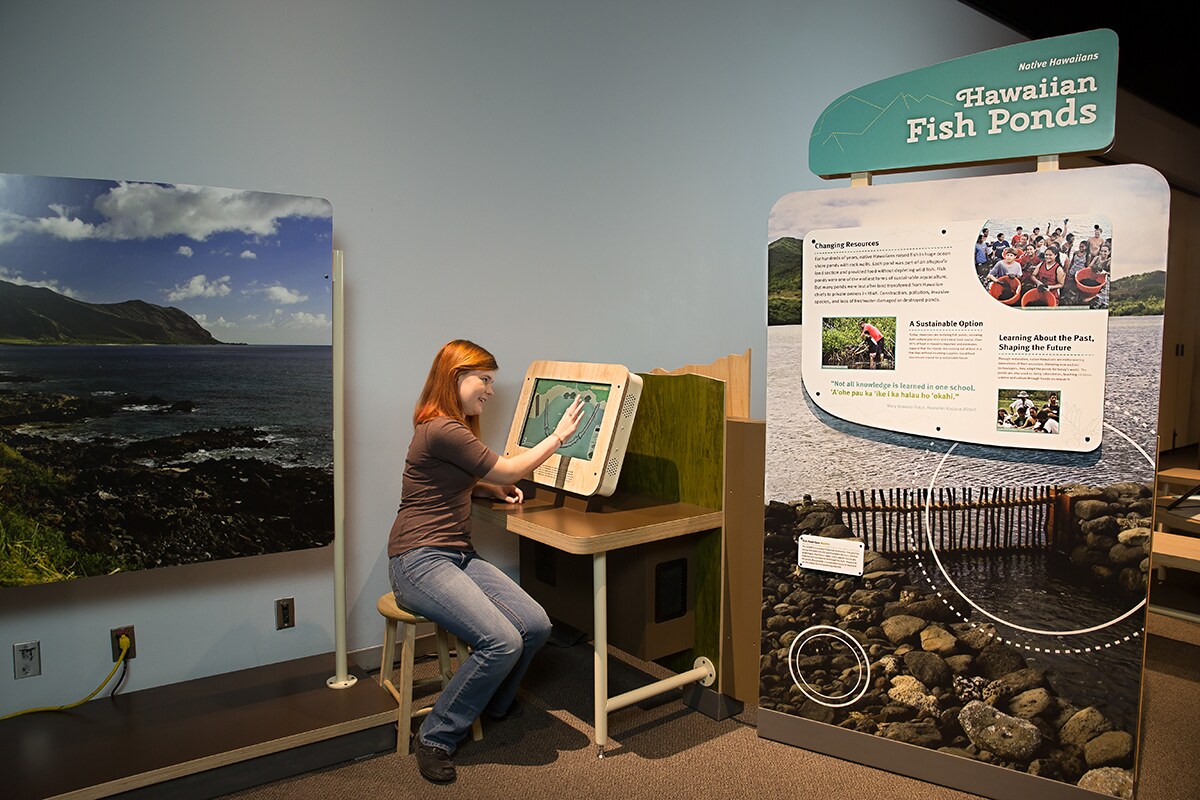 Female interacting with a digital screen in the Hawaiian Fish Pond exhibit.