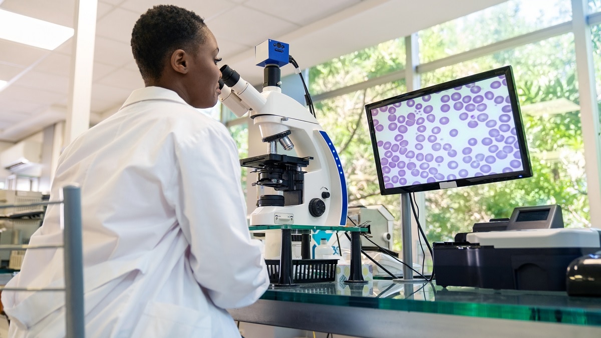 A pathology laboratory technician looking at a specimen under a microscope