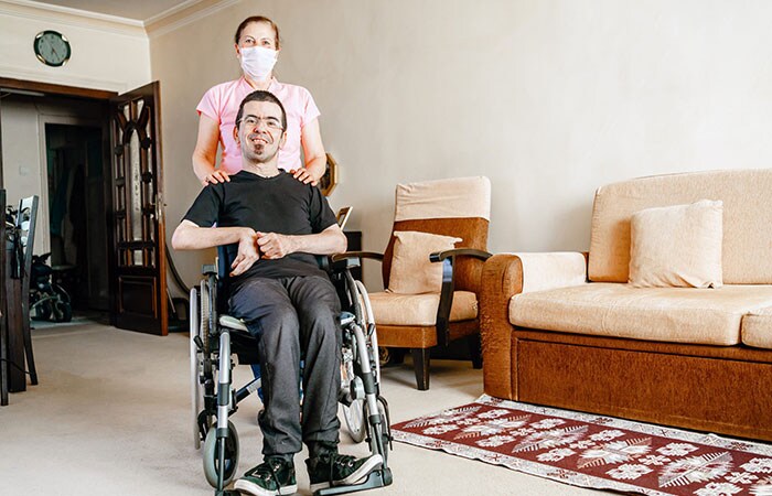 Hombre sonriendo en silla de ruedas con una mujer de pie detrás de él con una máscara protectora.