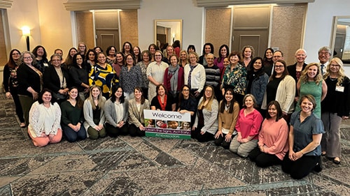 A group of Act Early Ambassadors gather around a sign that reads, "Welcome Learn the Signs. Act Early. Ambassadors."