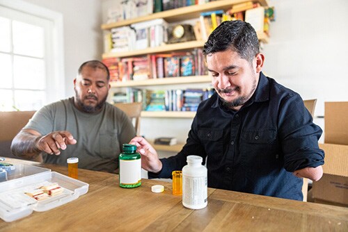 Two men sit at a table and prepare emergency supplies. One man has an amputated arm.