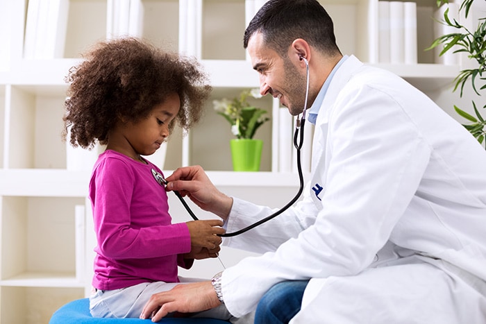 Doctor bending down to listen to a little girl's heart