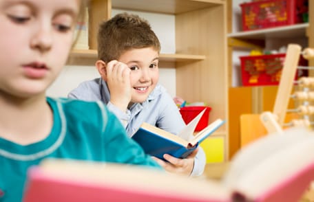 Boy looking up from book at a girl reading a book.