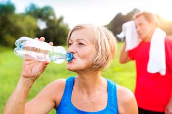 Una mujer mayor al aire libre bebiendo agua de una botella con un hombre mayor que se seca la cabeza con una toalla.